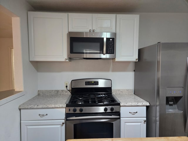 kitchen with stainless steel appliances, light stone countertops, and white cabinets