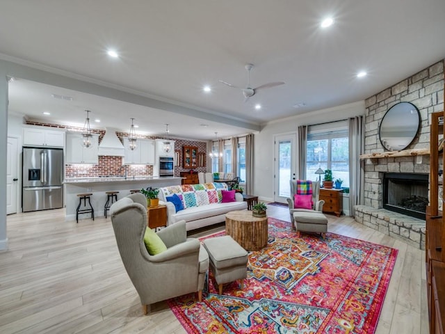 living room with crown molding, ceiling fan, a stone fireplace, and light hardwood / wood-style floors