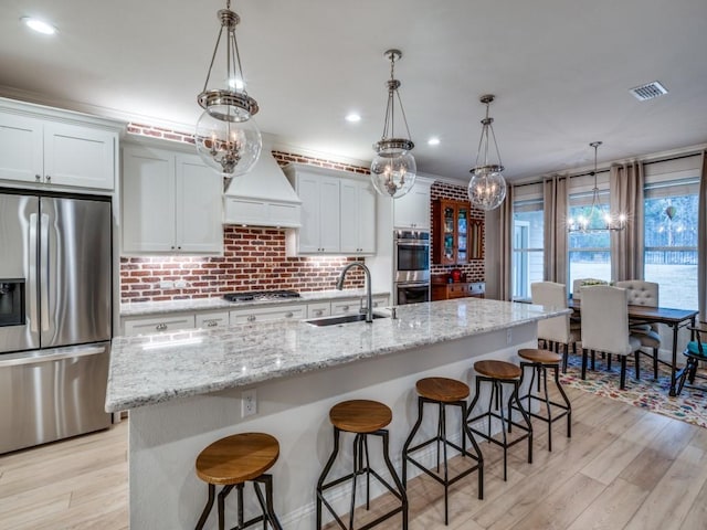 kitchen with decorative light fixtures, white cabinetry, sink, a kitchen island with sink, and stainless steel appliances