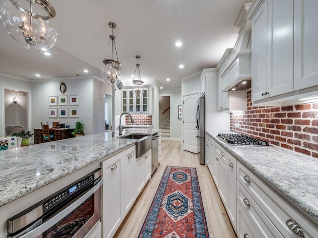 kitchen with sink, light stone counters, decorative light fixtures, appliances with stainless steel finishes, and white cabinets