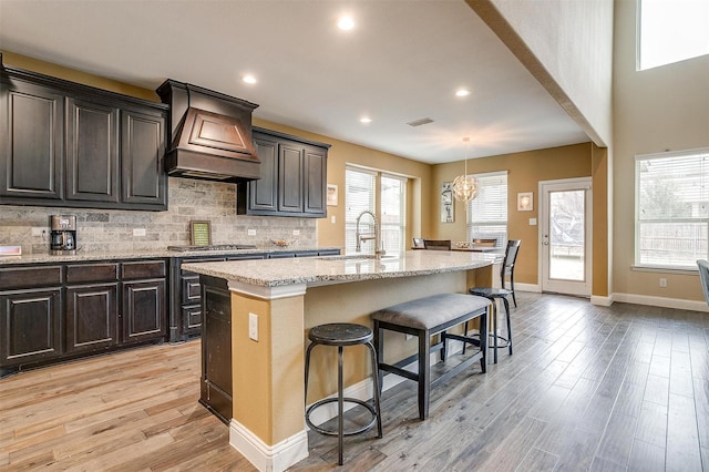 kitchen featuring a kitchen bar, sink, custom exhaust hood, a kitchen island with sink, and decorative backsplash