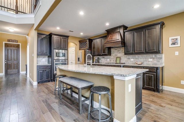 kitchen with sink, a breakfast bar area, a center island with sink, light wood-type flooring, and appliances with stainless steel finishes