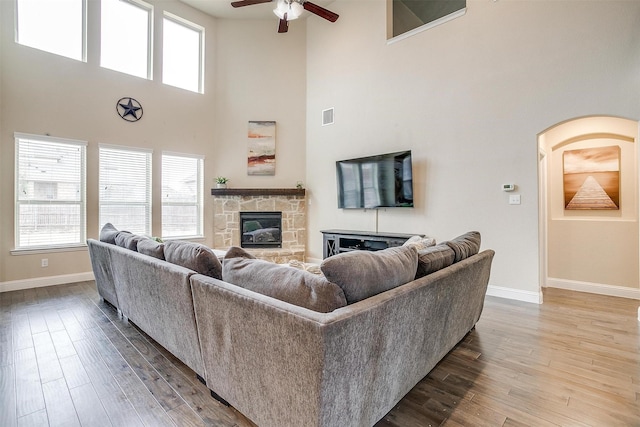 living room with ceiling fan, wood-type flooring, and a stone fireplace