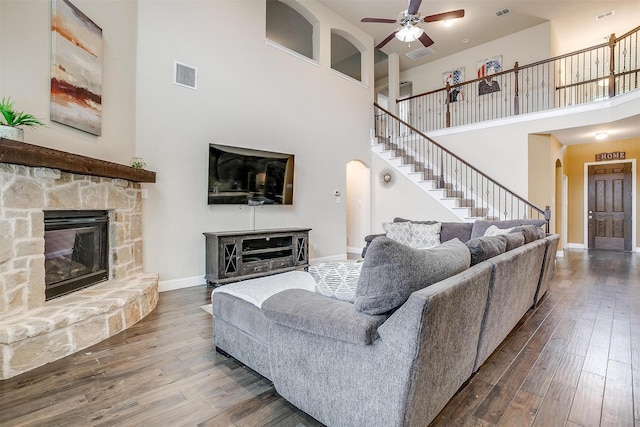 living room featuring a high ceiling, wood-type flooring, ceiling fan, and a fireplace