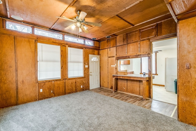 kitchen featuring ceiling fan, light colored carpet, and wood walls