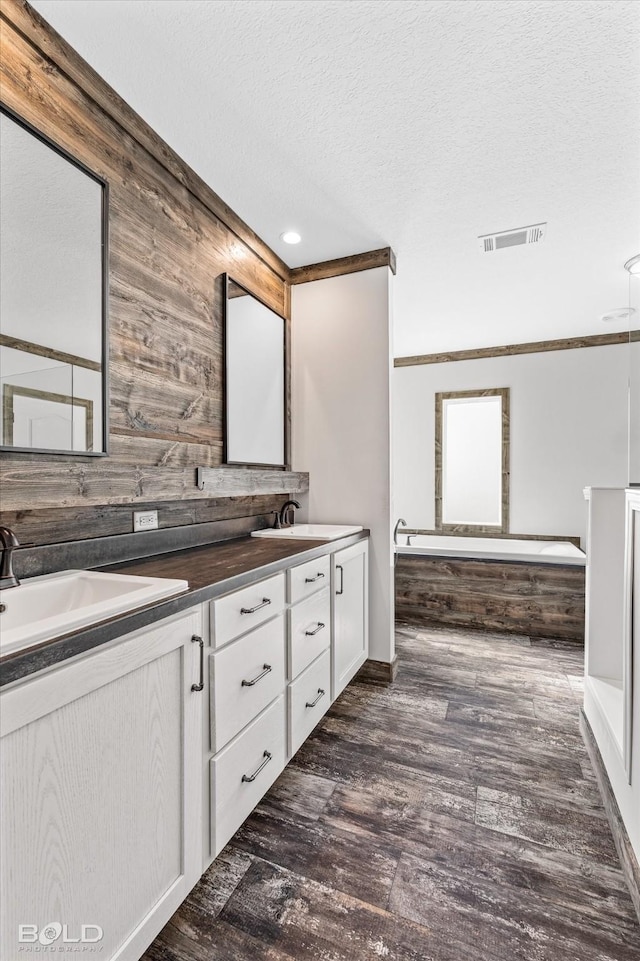 bathroom featuring hardwood / wood-style flooring, vanity, a textured ceiling, a bathing tub, and wood walls