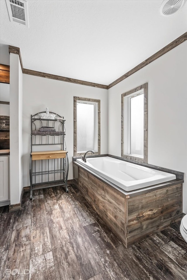 bathroom with crown molding, wood-type flooring, a textured ceiling, and tiled tub