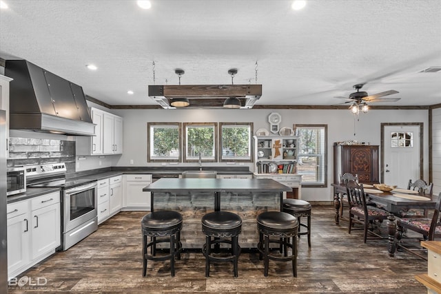 kitchen featuring appliances with stainless steel finishes, custom range hood, white cabinets, a kitchen island, and decorative light fixtures