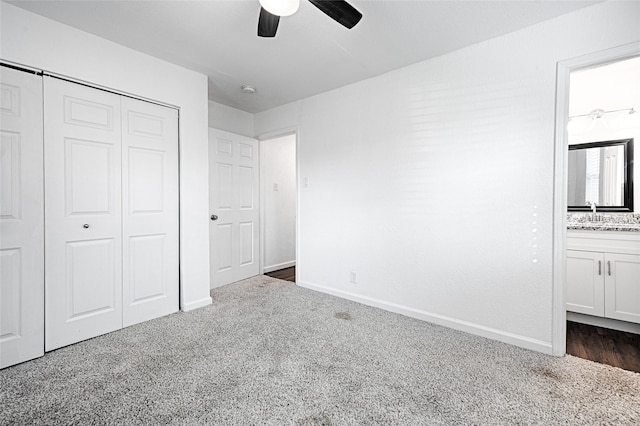 unfurnished bedroom with ensuite bathroom, a ceiling fan, baseboards, a closet, and dark colored carpet