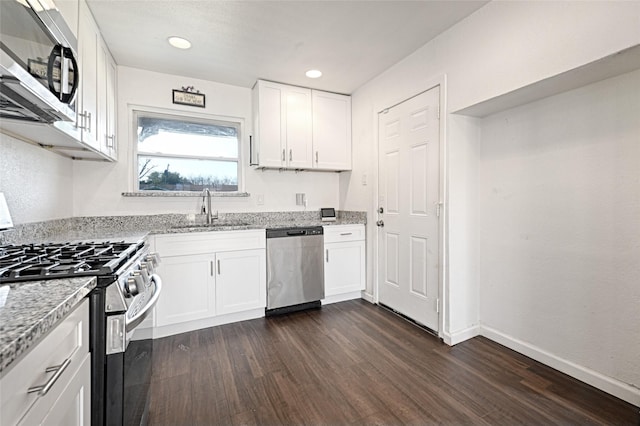 kitchen with light stone counters, a sink, white cabinetry, appliances with stainless steel finishes, and dark wood finished floors