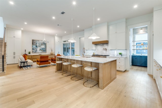 kitchen with white cabinetry, sink, hanging light fixtures, a large island, and light stone counters