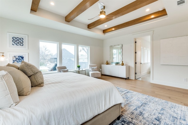 bedroom with ensuite bath, beamed ceiling, ceiling fan, a raised ceiling, and light wood-type flooring