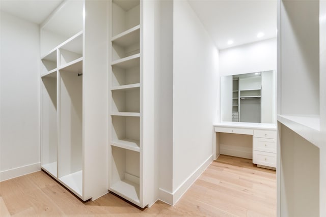 walk in closet with built in desk and light wood-type flooring