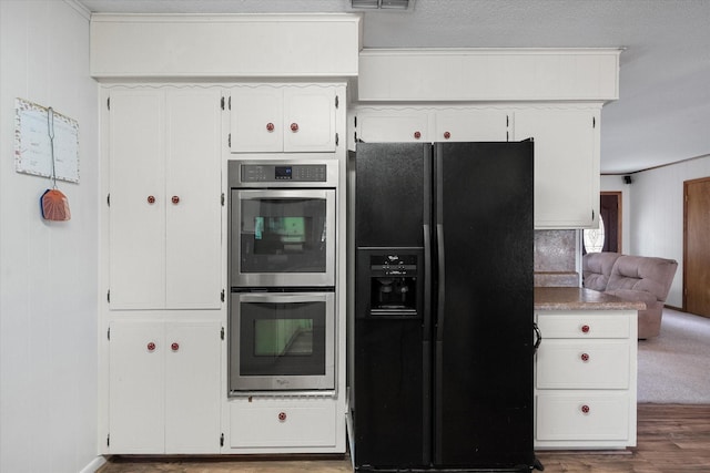 kitchen featuring white cabinetry, hardwood / wood-style floors, stainless steel double oven, and black fridge