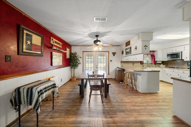 dining space featuring sink, ceiling fan, a textured ceiling, french doors, and light wood-type flooring