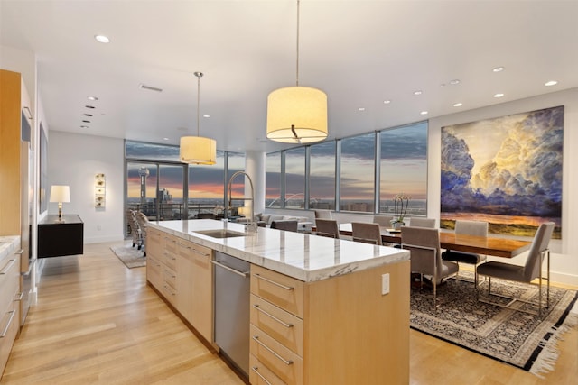 kitchen featuring sink, light stone counters, an island with sink, light brown cabinetry, and decorative light fixtures