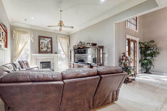 living room with a tiled fireplace, ceiling fan, ornamental molding, and a textured ceiling