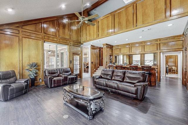 living room with ceiling fan, wooden walls, and high vaulted ceiling