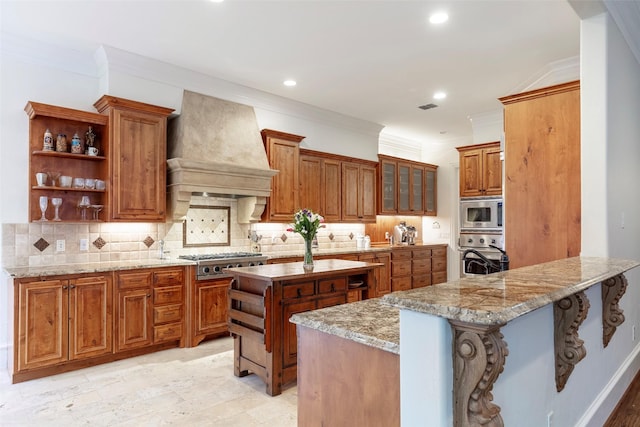 kitchen with a breakfast bar area, stainless steel appliances, light stone countertops, custom exhaust hood, and kitchen peninsula