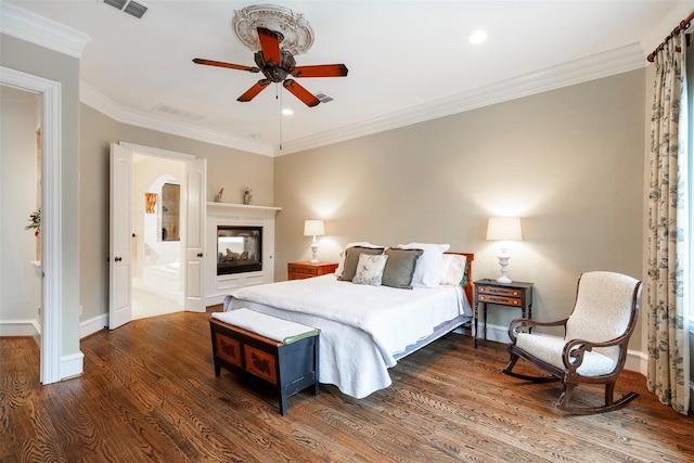 bedroom featuring a multi sided fireplace, ensuite bathroom, dark hardwood / wood-style floors, ceiling fan, and crown molding