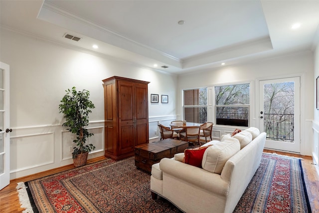 living room featuring crown molding, wood-type flooring, and a raised ceiling