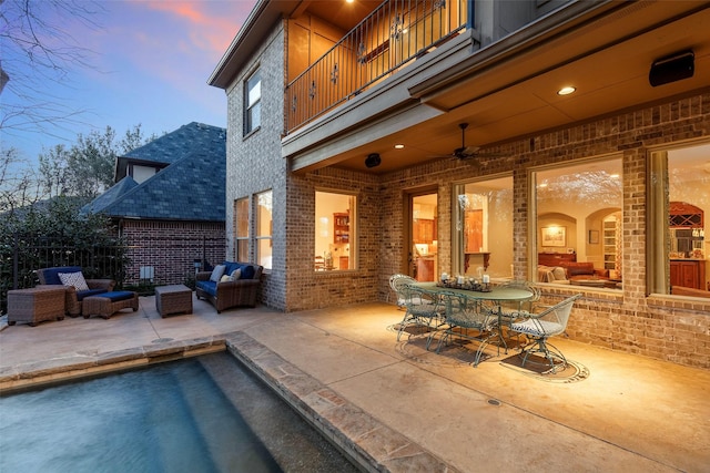 pool at dusk featuring ceiling fan, an outdoor hangout area, and a patio area