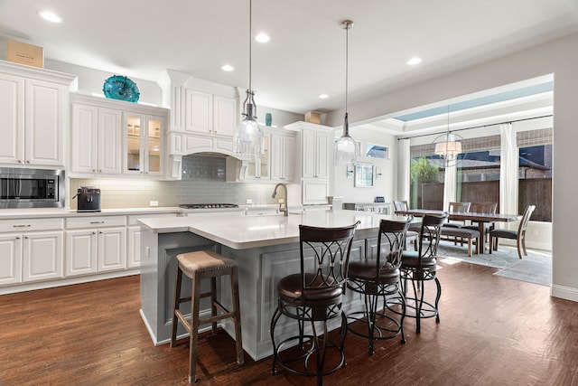 kitchen with pendant lighting, a kitchen island with sink, stainless steel microwave, and white cabinets