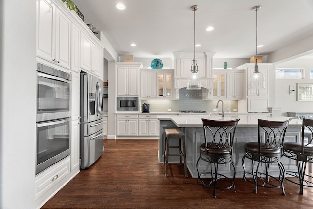 kitchen with decorative light fixtures, white cabinets, backsplash, a kitchen island with sink, and stainless steel appliances