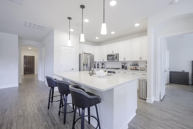 kitchen featuring appliances with stainless steel finishes, pendant lighting, an island with sink, white cabinets, and a kitchen bar