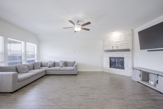 living room featuring ceiling fan, lofted ceiling, a stone fireplace, and light hardwood / wood-style flooring