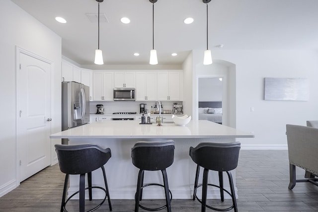 kitchen featuring white cabinetry, pendant lighting, stainless steel appliances, and an island with sink