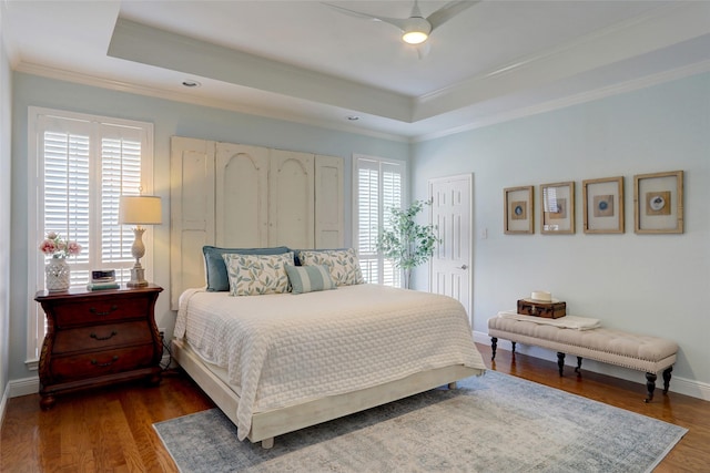 bedroom with ornamental molding, ceiling fan, dark hardwood / wood-style flooring, and a tray ceiling