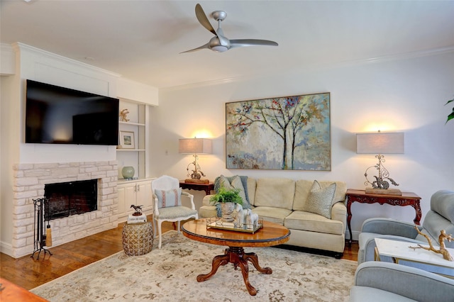 living room with wood-type flooring, a stone fireplace, ornamental molding, and ceiling fan