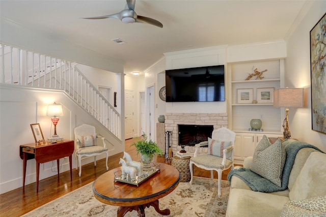 living room featuring ornate columns, a stone fireplace, wood-type flooring, ornamental molding, and ceiling fan