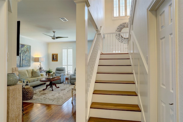 stairway featuring hardwood / wood-style flooring, ceiling fan, and ornate columns