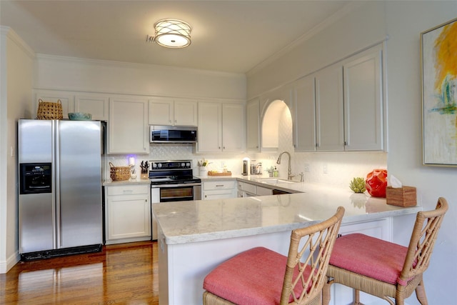 kitchen with a kitchen bar, sink, appliances with stainless steel finishes, kitchen peninsula, and white cabinets