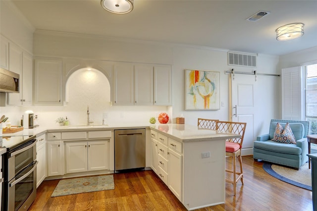 kitchen featuring sink, white cabinetry, appliances with stainless steel finishes, kitchen peninsula, and a barn door