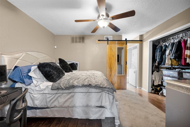 bedroom featuring ceiling fan, wood-type flooring, a textured ceiling, a barn door, and a closet