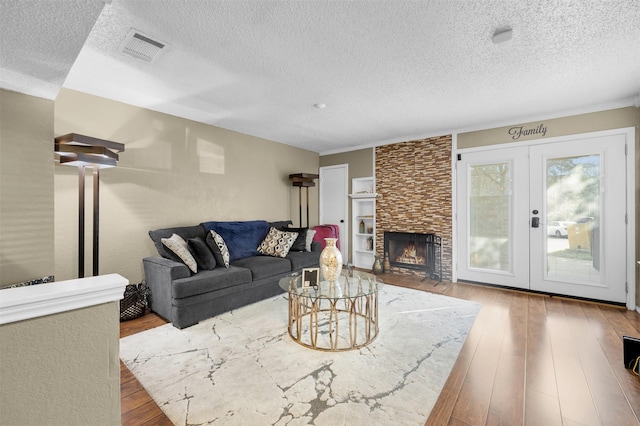 living room with french doors, wood-type flooring, a fireplace, and a textured ceiling