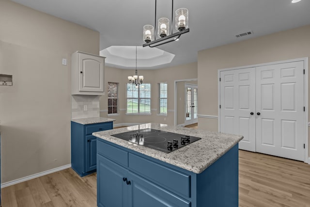 kitchen featuring a kitchen island, blue cabinets, black electric stovetop, a raised ceiling, and an inviting chandelier