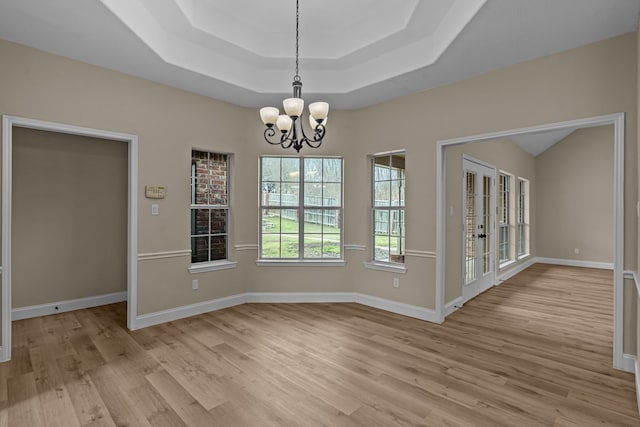 unfurnished dining area featuring a raised ceiling, french doors, a chandelier, and light hardwood / wood-style flooring