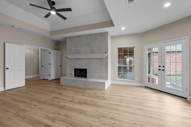 unfurnished living room featuring a tiled fireplace, light hardwood / wood-style flooring, french doors, and a raised ceiling