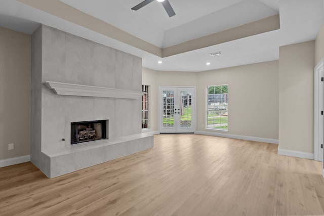 unfurnished living room with a fireplace, light hardwood / wood-style flooring, french doors, and a raised ceiling