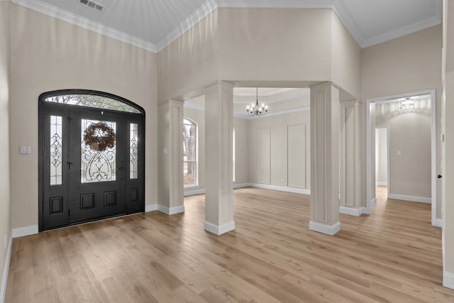 foyer entrance featuring ornate columns, crown molding, a chandelier, light wood-type flooring, and a high ceiling