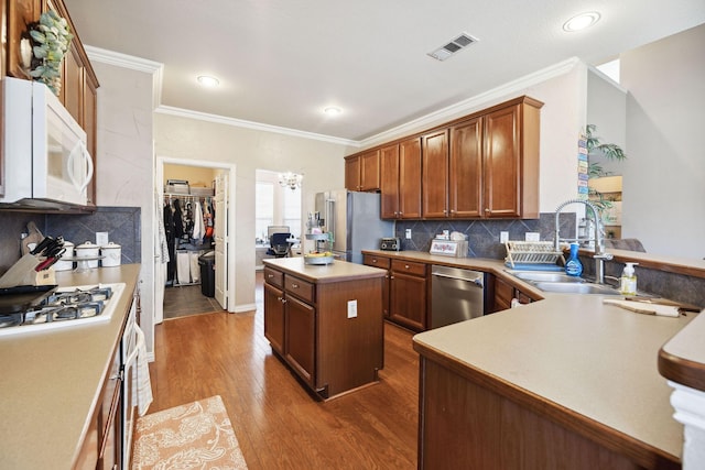 kitchen with sink, stainless steel appliances, wood-type flooring, a kitchen island, and decorative backsplash