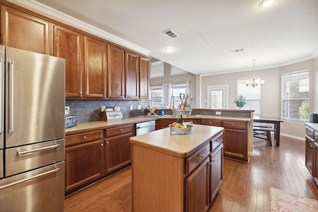 kitchen featuring appliances with stainless steel finishes, hanging light fixtures, wood-type flooring, a kitchen island, and decorative backsplash