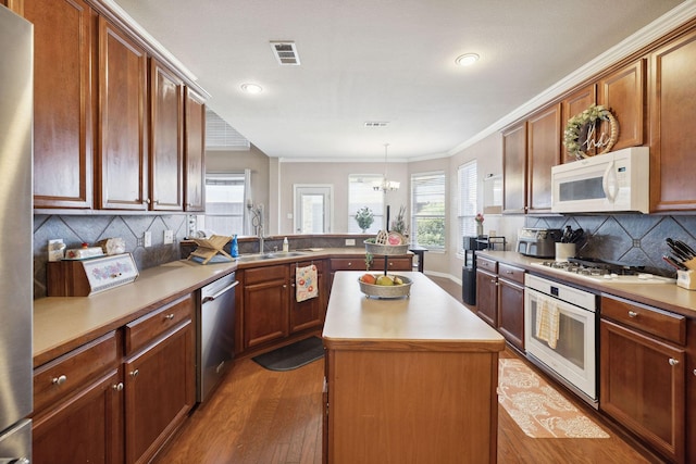 kitchen featuring appliances with stainless steel finishes, dark hardwood / wood-style floors, decorative light fixtures, sink, and a center island