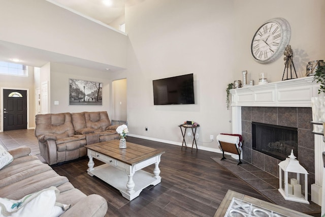 living room with dark wood-type flooring, a tiled fireplace, and a high ceiling