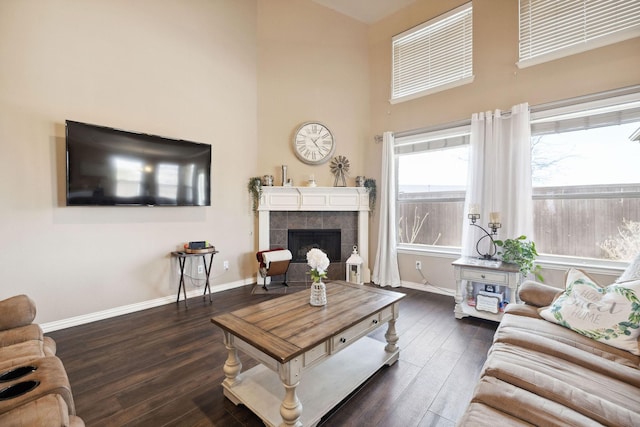 living room featuring a tiled fireplace, dark wood-type flooring, and a towering ceiling