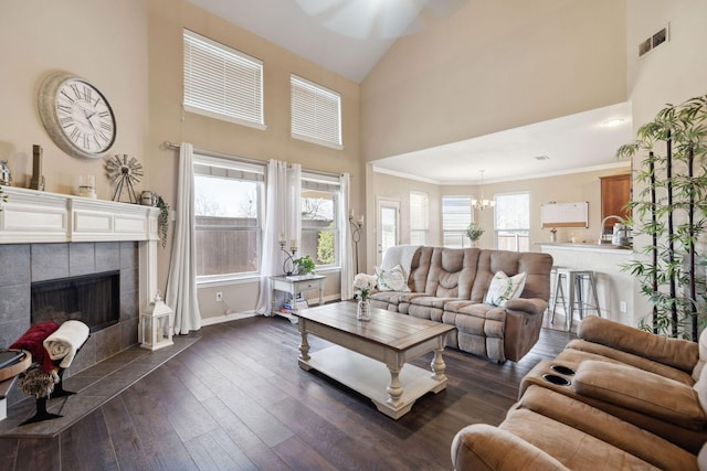 living room featuring crown molding, high vaulted ceiling, dark hardwood / wood-style flooring, a notable chandelier, and a fireplace